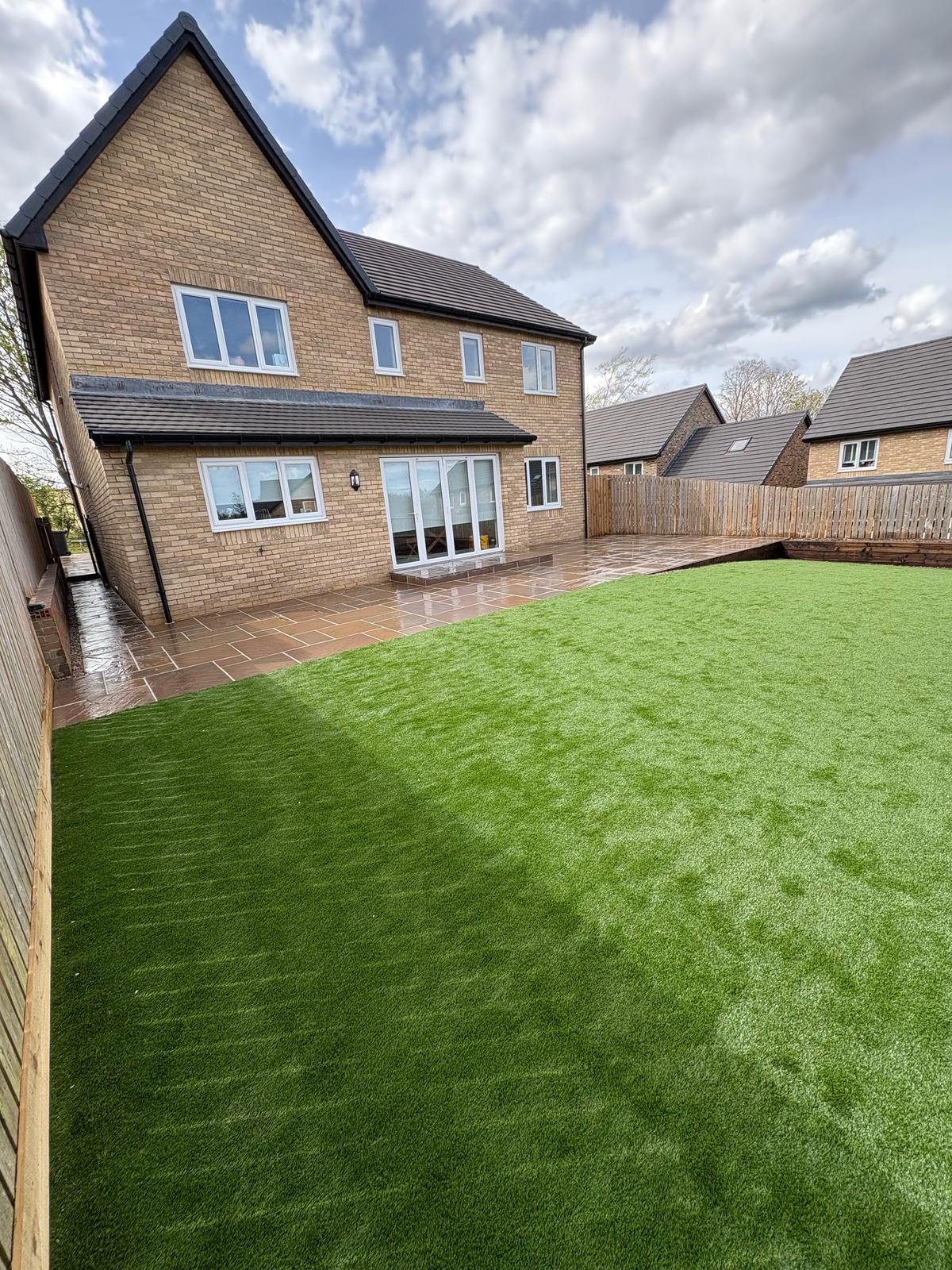 A large artificial lawn and riven sandstone patio laid behind a new build house in Durham